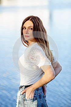 Beautiful brunette girl in a white T-shirt and jeans near the river. Summer. Relax.