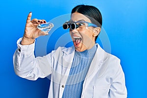 Beautiful brunette jeweller woman holding brilliant diamond stone wearing magnifier glasses celebrating crazy and amazed for