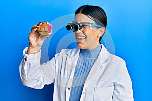Beautiful brunette jeweller woman holding geode stone wearing magnifier glasses smiling with a happy and cool smile on face