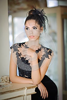 Beautiful brunette lady in elegant black lace dress posing in a vintage scene. Young sensual fashionable woman