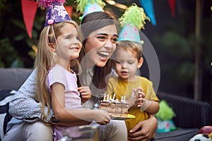 Beautiful brunette laughing between little girl and boy with extinguished candles on birthday cake