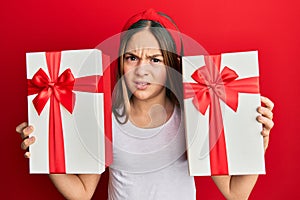 Beautiful brunette little girl holding gifts clueless and confused expression