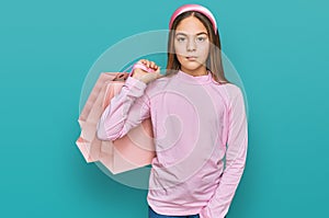 Beautiful brunette little girl holding shopping bags thinking attitude and sober expression looking self confident