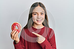 Beautiful brunette little girl holding tasty colorful doughnut smiling happy pointing with hand and finger