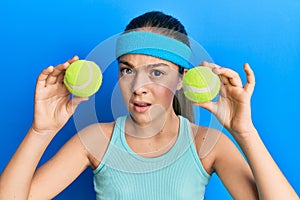 Beautiful brunette little girl holding tennis ball close to eyes clueless and confused expression
