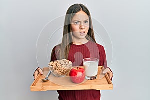 Beautiful brunette little girl holding tray with breakfast food clueless and confused expression