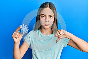 Beautiful brunette little girl holding virus toy with angry face, negative sign showing dislike with thumbs down, rejection