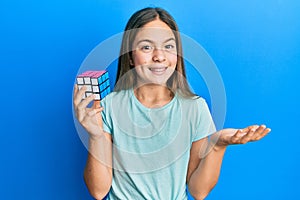 Beautiful brunette little girl playing colorful puzzle cube intelligence game celebrating achievement with happy smile and winner