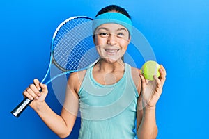 Beautiful brunette little girl playing tennis holding racket and ball celebrating crazy and amazed for success with open eyes