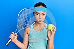 Beautiful brunette little girl playing tennis holding racket and ball skeptic and nervous, frowning upset because of problem