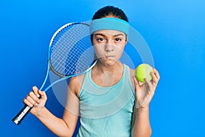 Beautiful brunette little girl playing tennis holding racket and ball skeptic and nervous, frowning upset because of problem