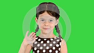 Beautiful brunette little girl in polka dot dress waving to the camera on a Green Screen, Chroma Key.