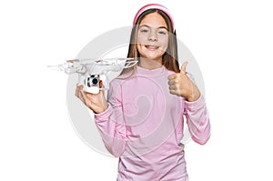 Beautiful brunette little girl using drone smiling happy and positive, thumb up doing excellent and approval sign