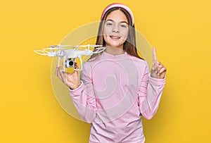 Beautiful brunette little girl using drone surprised with an idea or question pointing finger with happy face, number one