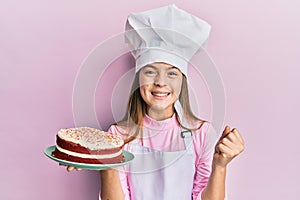 Beautiful brunette little girl wearing baker uniform holding homemade cake screaming proud, celebrating victory and success very