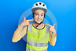 Beautiful brunette little girl wearing bike helmet and reflective vest smiling cheerful showing and pointing with fingers teeth