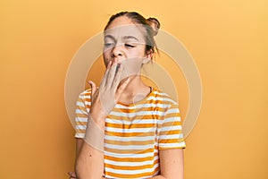 Beautiful brunette little girl wearing casual striped t shirt bored yawning tired covering mouth with hand