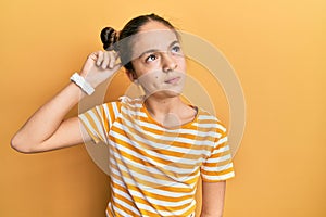 Beautiful brunette little girl wearing casual striped t shirt confuse and wondering about question