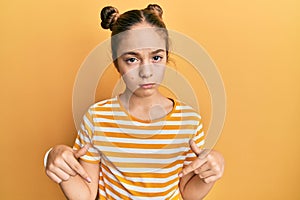 Beautiful brunette little girl wearing casual striped t shirt pointing down looking sad and upset, indicating direction with