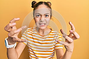Beautiful brunette little girl wearing casual striped t shirt shouting frustrated with rage, hands trying to strangle, yelling mad