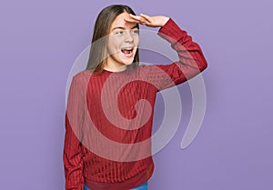 Beautiful brunette little girl wearing casual sweater very happy and smiling looking far away with hand over head