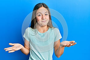 Beautiful brunette little girl wearing casual white t shirt clueless and confused expression with arms and hands raised