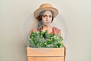 Beautiful brunette little girl wearing gardener hat holding wooden plant pot clueless and confused expression