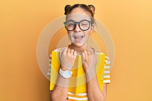 Beautiful brunette little girl wearing glasses and holding book winking looking at the camera with expression, cheerful and