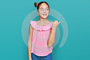 Beautiful brunette little girl wearing summer pink shirt smiling with happy face looking and pointing to the side with thumb up