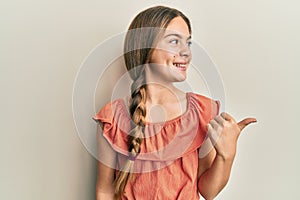 Beautiful brunette little girl wearing summer shirt pointing thumb up to the side smiling happy with open mouth