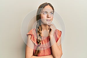 Beautiful brunette little girl wearing summer shirt thinking concentrated about doubt with finger on chin and looking up wondering