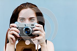 Beautiful brunette with long hair looking at the camera and holding in hands vintage camera. Close up.