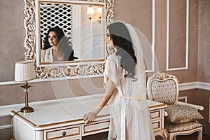 Beautiful and brunette model girl in fashionable peignoir looking in the mirror on her reflexion at classic