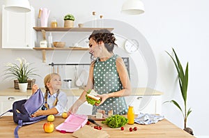 Beautiful brunette mother and her daughter packing healthy lunch and preparing school bag