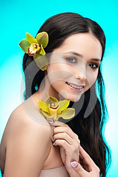 A beautiful brunette nude shoulders girl sensually holds a flower of an orchid in her hands. Nude make-up. Healthy smooth skin