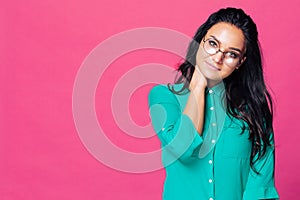 A beautiful brunette on a pink background with glasses touches her neck