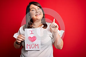 Beautiful brunette plus size woman holding love mom message celebrating mothers day surprised with an idea or question pointing