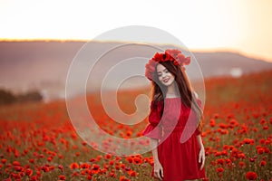 Beautiful brunette in red poppies field. Happy smiling teen girl portrait with wreath on head enjoying in poppy flowers nature