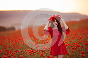 Beautiful brunette in red poppies field. Happy smiling teen girl portrait with wreath on head enjoying in poppy flowers nature