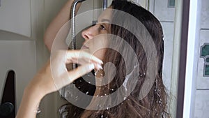 Beautiful brunette in shower wetting long dry hair from shower head. slow motion