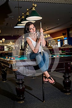 Beautiful brunette sitting on billiard table with cue