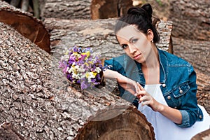 Beautiful brunette sitting on logs with flowers