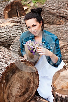 Beautiful brunette sitting on logs with flowers