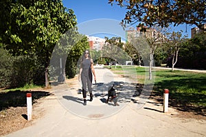 beautiful and brunette Spanish woman is walking her dog which is a Doberman puppy. The woman is dressed in very elegant black.