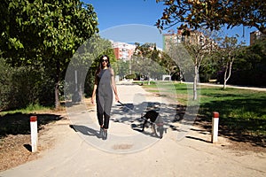 beautiful and brunette Spanish woman is walking her dog which is a Doberman puppy. The woman is dressed in very elegant black.