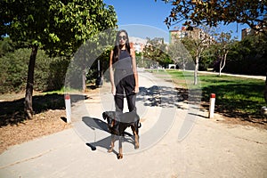 beautiful and brunette Spanish woman is walking her dog which is a Doberman puppy. The woman is dressed in very elegant black.