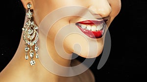 Beautiful brunette woman with bright make-up and jewelry earrings smiling close-up. Red lips and nails, evening make-up