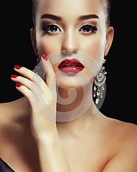 Beautiful brunette woman with bright make-up and jewelry earrings smiling close-up. Red lips and nails, evening make-up