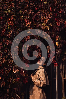 a beautiful brunette woman in a coat by the hedge braided with autumn vines.