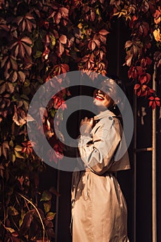 a beautiful brunette woman in a coat by the hedge braided with autumn vines.